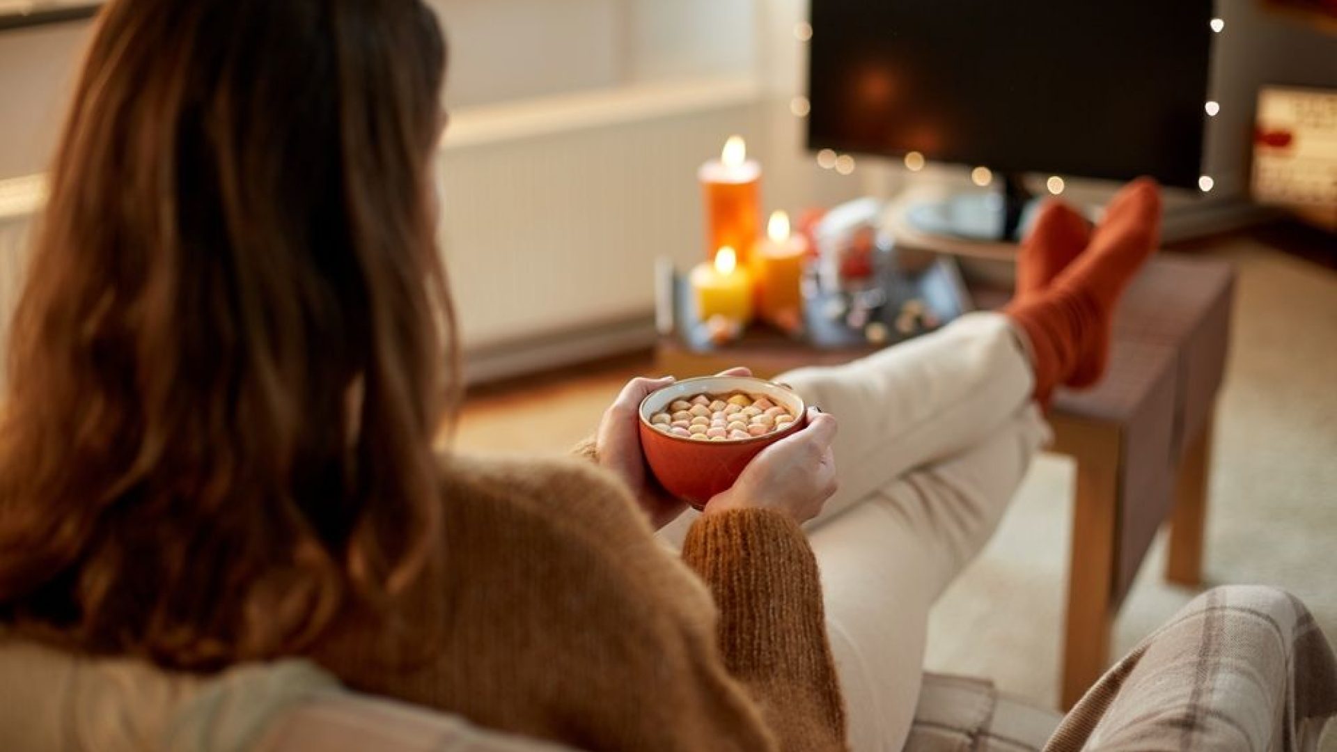 cioccolata.jpg halloween, holidays and leisure concept - young woman watching tv and drinking hot chocolate with marshmallow with her feet on table at cozy home