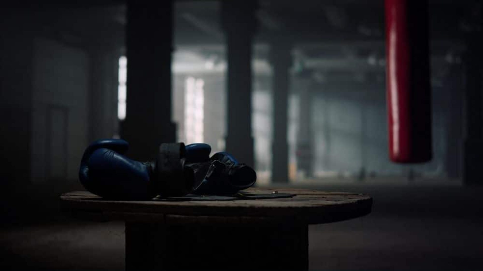 Box sport concept. Closeup boxing gloves lying on wooden box in empty gym. Fitness equipment in sport club. Modern gym with punching bag for boxing training on background.