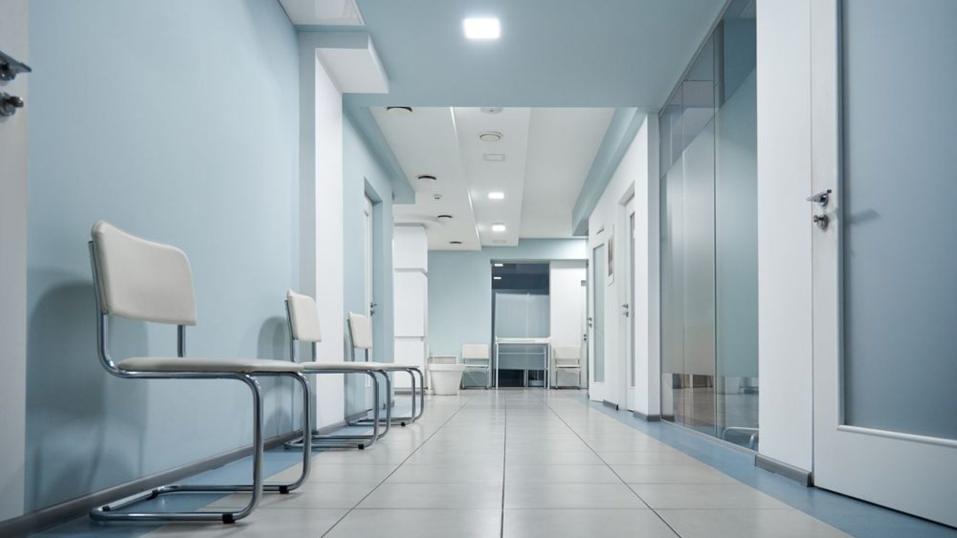 Empty modern hospital corridor, clinic hallway interior background with white chairs for patients waiting for doctor visit. Contemporary waiting room in medical office. Healthcare services concept
